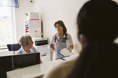 Female doctor discussing with senior nurse while looking at patient in medical clinic