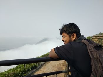 Side view of young man standing by railing on mountain peak