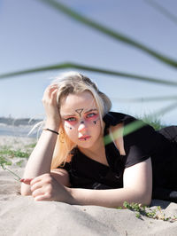 Portrait of young woman lying down on land against sky