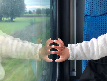 Close-up of hand holding glass window of train