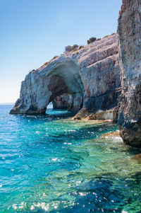 Rock formations by sea against clear blue sky