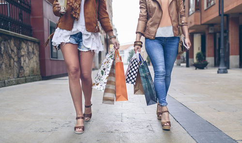 Low section of two women holding shopping bags walking in the city