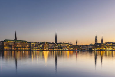 View of illuminated buildings by river against sky in city