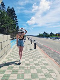 Rear view on woman wearing hat while walking on sidewalk during sunny day