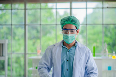 Portrait of scientist wearing surgical mask and cap standing in laboratory