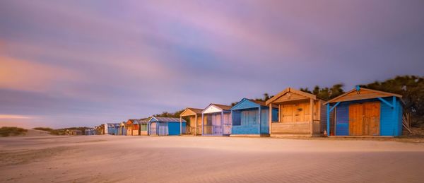 Houses on beach by buildings against sky during sunset