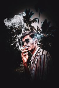 Portrait of young man smoking cigarette against black background