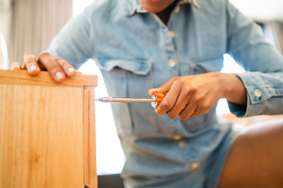 Midsection of woman holding screw driver while repairing furniture at home