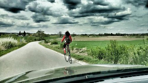 Rear view of man walking on road against cloudy sky