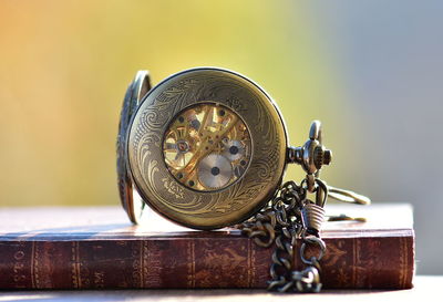 Close-up of pocket watch on book during sunny day