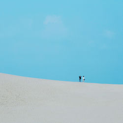 Low angle view of men standing on sand dunes against sky
