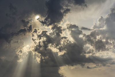 Low angle view of sunlight streaming through clouds