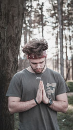 Young man praying by trees on field