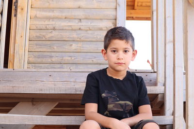 Portrait of boy sitting on wooden wall