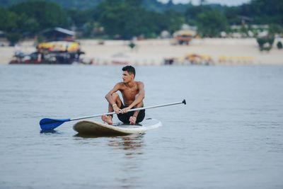 Full length of shirtless man sitting in sea