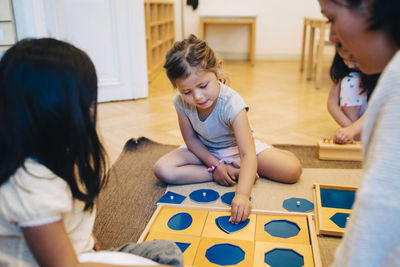 Teacher and student looking at girl playing puzzle game in classroom