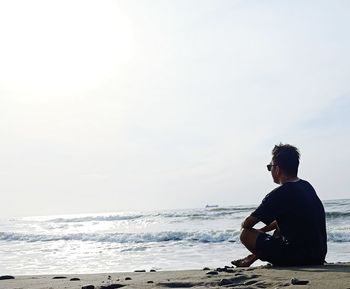 Side view of man standing at beach against sky