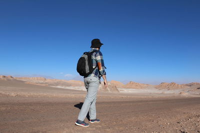 Rear view of backpack man walking on desert against clear blue sky