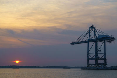 Silhouette cranes against sky at sunset