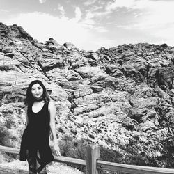 Portrait of smiling young woman standing on rock against sky