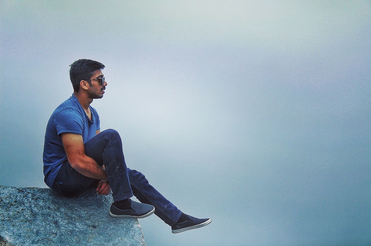 SIDE VIEW OF MAN SITTING ON BLUE WALL