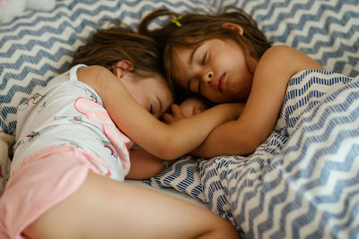 High angle view of sisters sleeping on bed