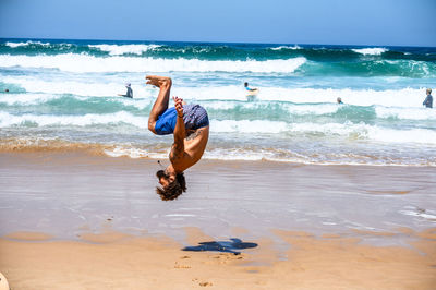 Full length of man jumping on beach against sky