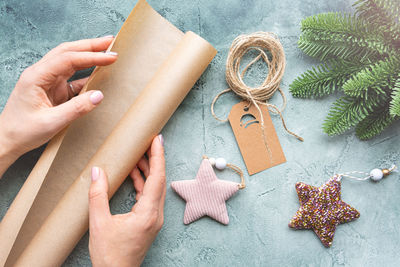 Close-up of hands holding a roll of wrapping craft paper on textured background with christmas toys.