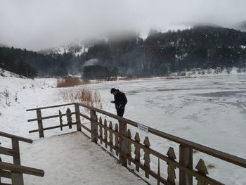 Man standing on railing against snowcapped mountain during winter