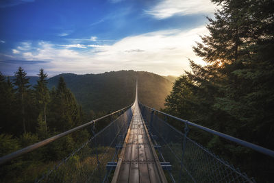 Empty suspension footbridge over mountains against sky