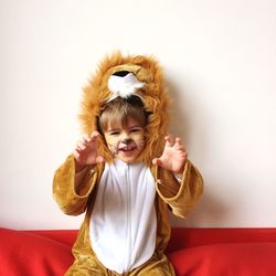 Portrait of boy gesturing in lion costume while sitting on sofa