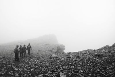 People walking on landscape against sky during foggy weather