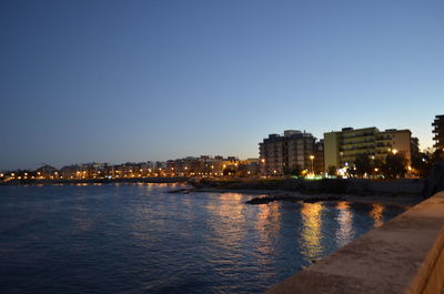 River by illuminated buildings against clear sky at dusk