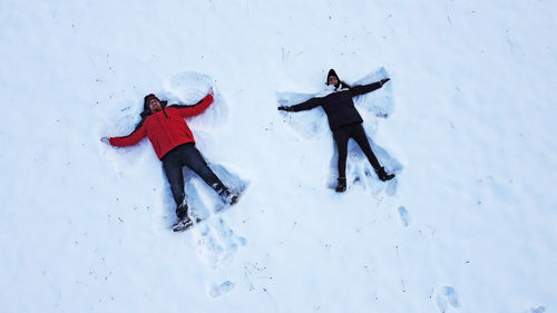 Aerial view of couple lying on snow covered land during winter