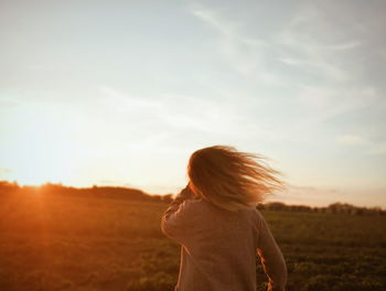 Rear view of girl standing on field during sunset