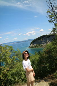 Young woman standing by plants against sky