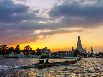 Scenic view of river by buildings against sky during sunset