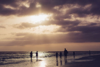 Silhouette people on beach against sky during sunset