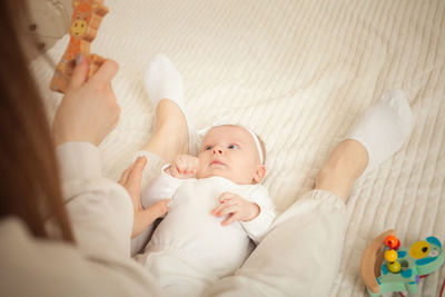 Child lies on bed, plays with toy, mother teaches her daughter, newborn baby in bedroom. 