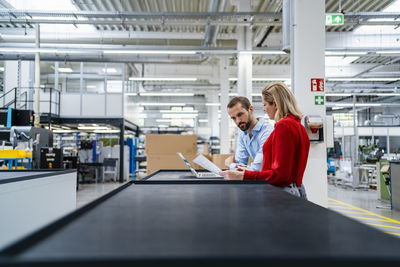 Business colleagues working on laptop at table in factory