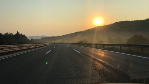 Road by mountains against sky during sunset