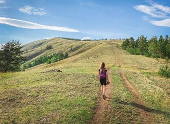 Rear view of woman walking on field against sky