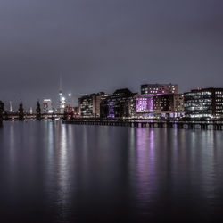 Illuminated buildings by river against sky at night