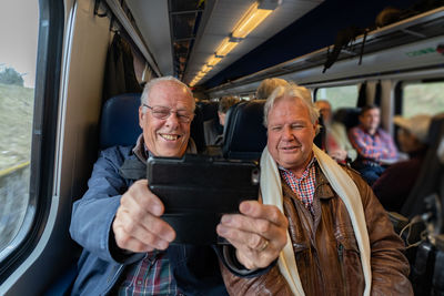 Smiling senior friends taking selfie while sitting in train