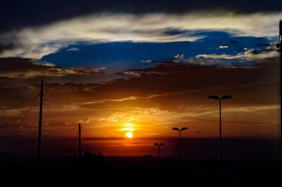 Silhouette street lights against dramatic sky during sunset