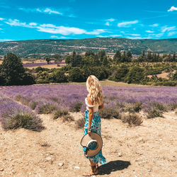 Full length of woman holding hat standing against landscape