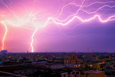 Lightning over illuminated cityscape against sky at night