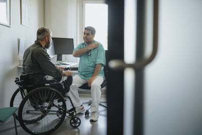 Doctor discussing with male patient sitting in wheelchair at clinic