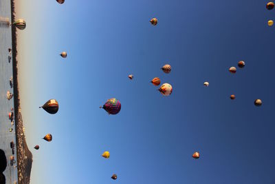 Tilt image of hot air balloons flying over sea against clear sky