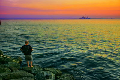 Man looking at sea against sky during sunset